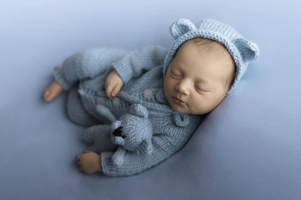 A newborn baby posinG on a blue background with the small toy